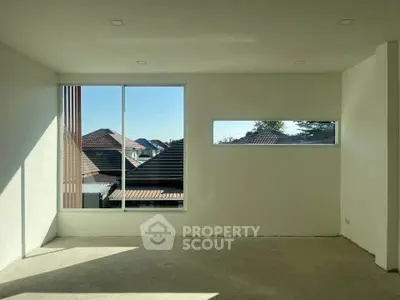 Spacious room with large windows offering a scenic view of rooftops, perfect for natural light lovers.