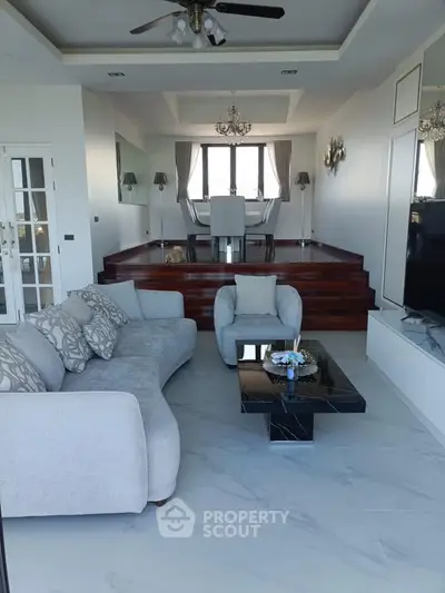 Luxurious living room with elegant decor and elevated dining area, featuring plush seating and marble flooring.