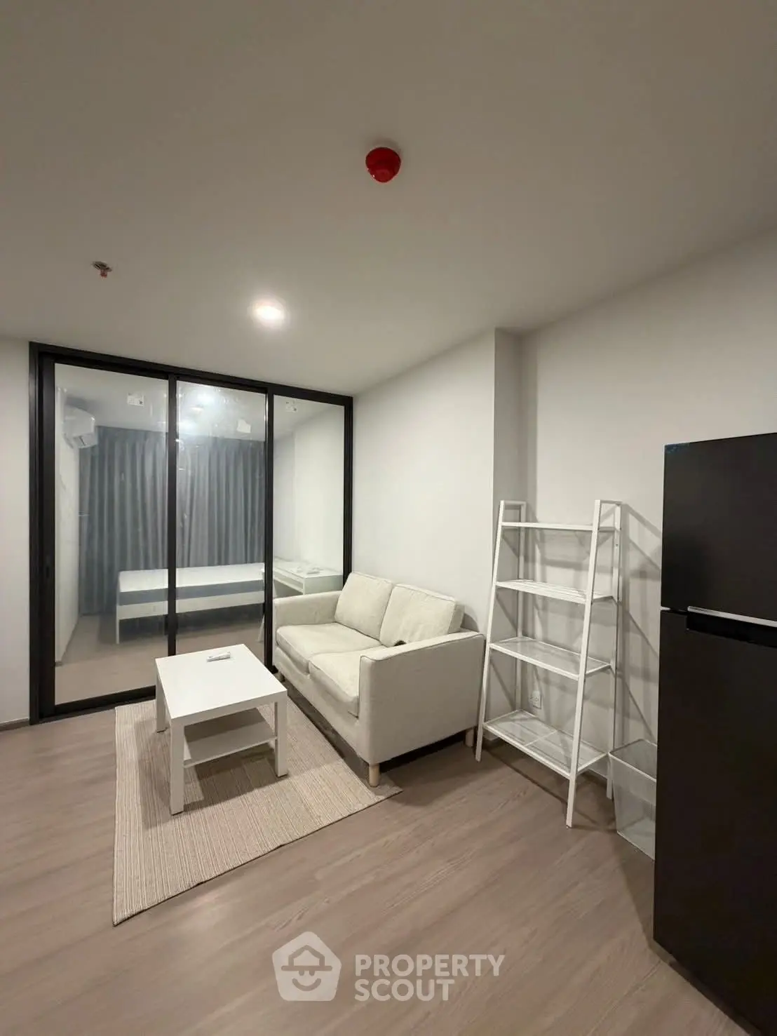 Modern living room with glass partition, cozy sofa, and sleek refrigerator in a minimalist apartment.