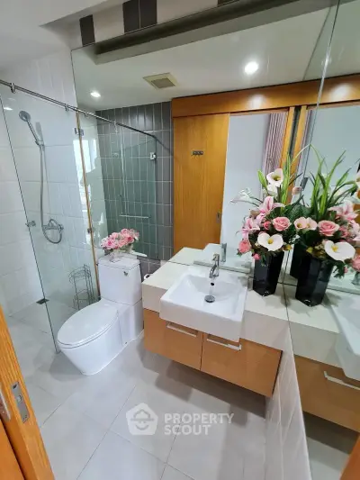 Modern bathroom with glass shower, elegant sink, and floral decor