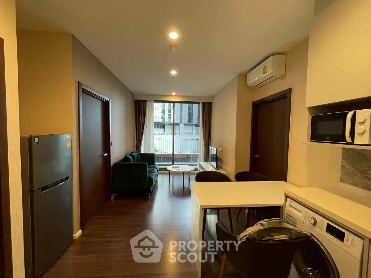 Modern apartment interior with open kitchen and living area, featuring washing machine and microwave.