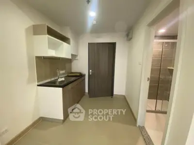 Modern compact kitchen with sleek cabinetry and adjacent bathroom entrance in a contemporary apartment.