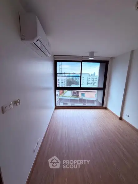 Spacious room with large window and city view, featuring modern air conditioning.