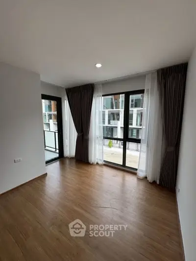 Spacious empty room with large windows and wooden flooring in modern apartment.