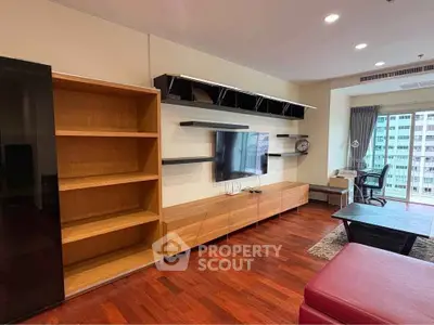 Spacious living room with modern TV setup and wooden flooring in high-rise apartment.