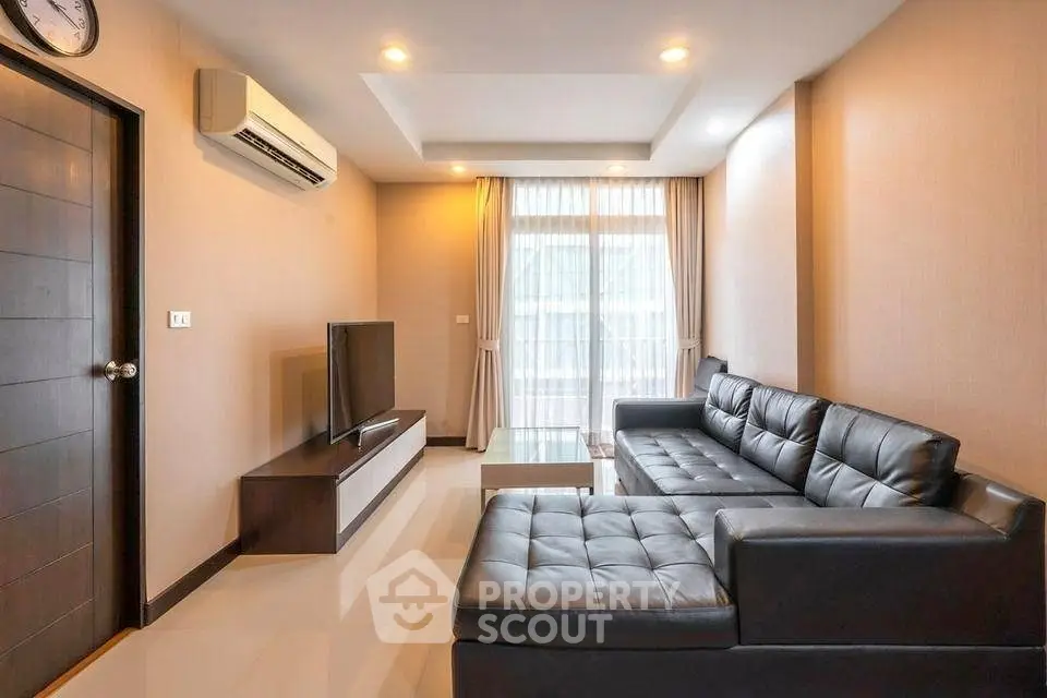 Modern living room with sleek black leather sofa and large TV, featuring elegant lighting and natural light from window.