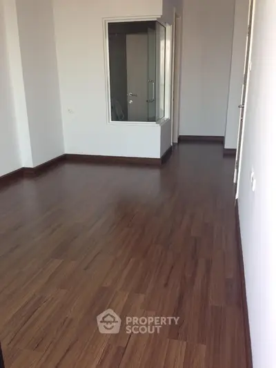 Spacious empty room with wooden flooring and glass shower enclosure.