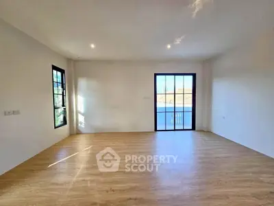 Spacious empty room with wooden flooring and large windows, perfect for customization.