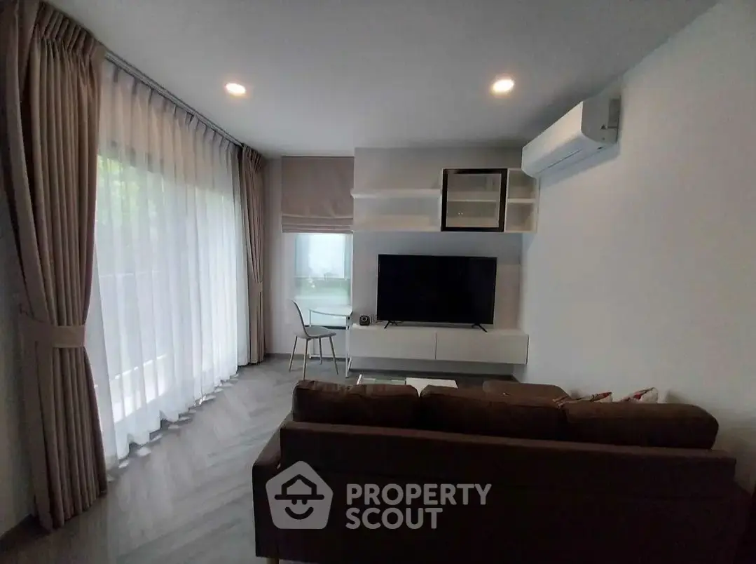 Modern living room with large window, stylish sofa, and wall-mounted TV in a cozy apartment.