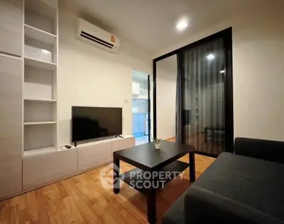 Modern living room with sleek furniture and wooden flooring, featuring a TV and air conditioning.