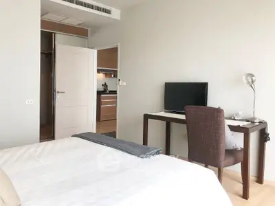 Modern bedroom with desk and TV, adjacent to a sleek kitchen area.