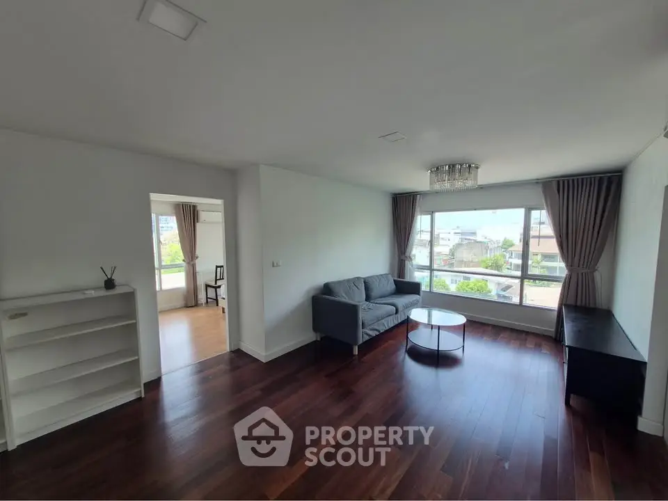 Spacious living room with hardwood floors and large window offering city views.