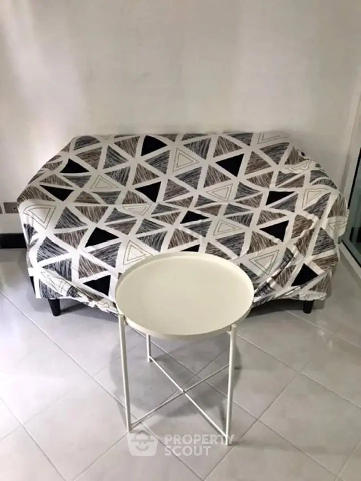Cozy living room with modern geometric-patterned sofa and sleek round table on tiled floor.