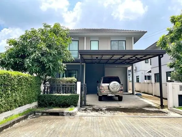Modern two-story house with carport and lush greenery in a serene neighborhood.