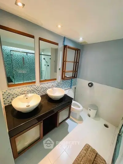 Modern bathroom with dual sinks and glass shower enclosure in stylish apartment.