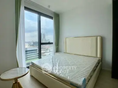 Modern bedroom with large window offering city view, featuring elegant bed and side table.