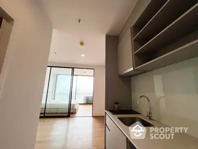 Modern kitchen with sleek white cabinetry and countertops, leading to a sunlit balcony with a clear glass door, perfect for urban living.