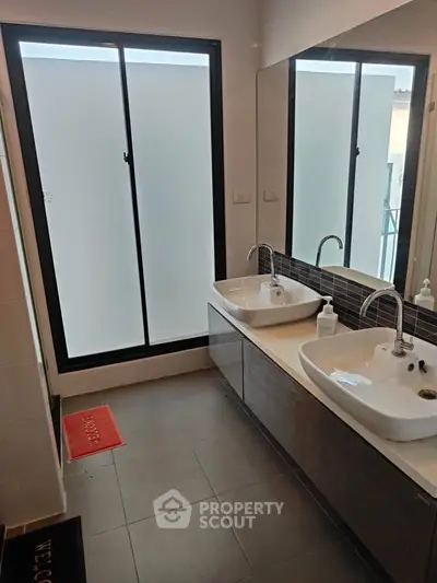 Modern bathroom with dual sinks and large frosted window, offering a sleek and functional design.