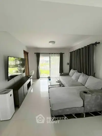 Modern living room with sleek gray sofa and large TV, bright natural light from window.