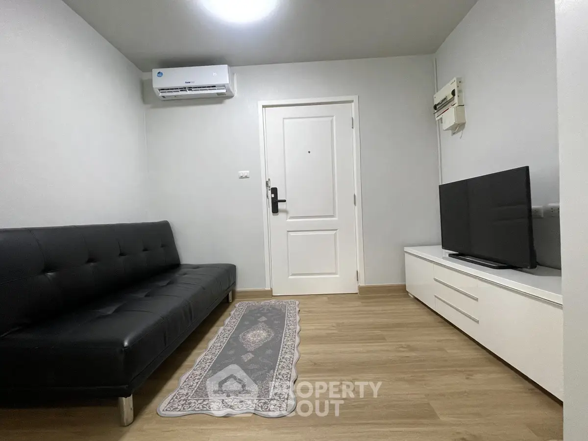 Modern living room with sleek black sofa and flat-screen TV, featuring minimalist decor and wooden flooring.