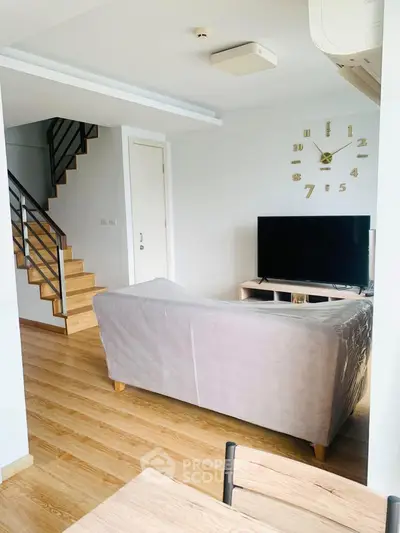 Modern living room with stylish staircase and wall clock, featuring a cozy sofa and flat-screen TV.