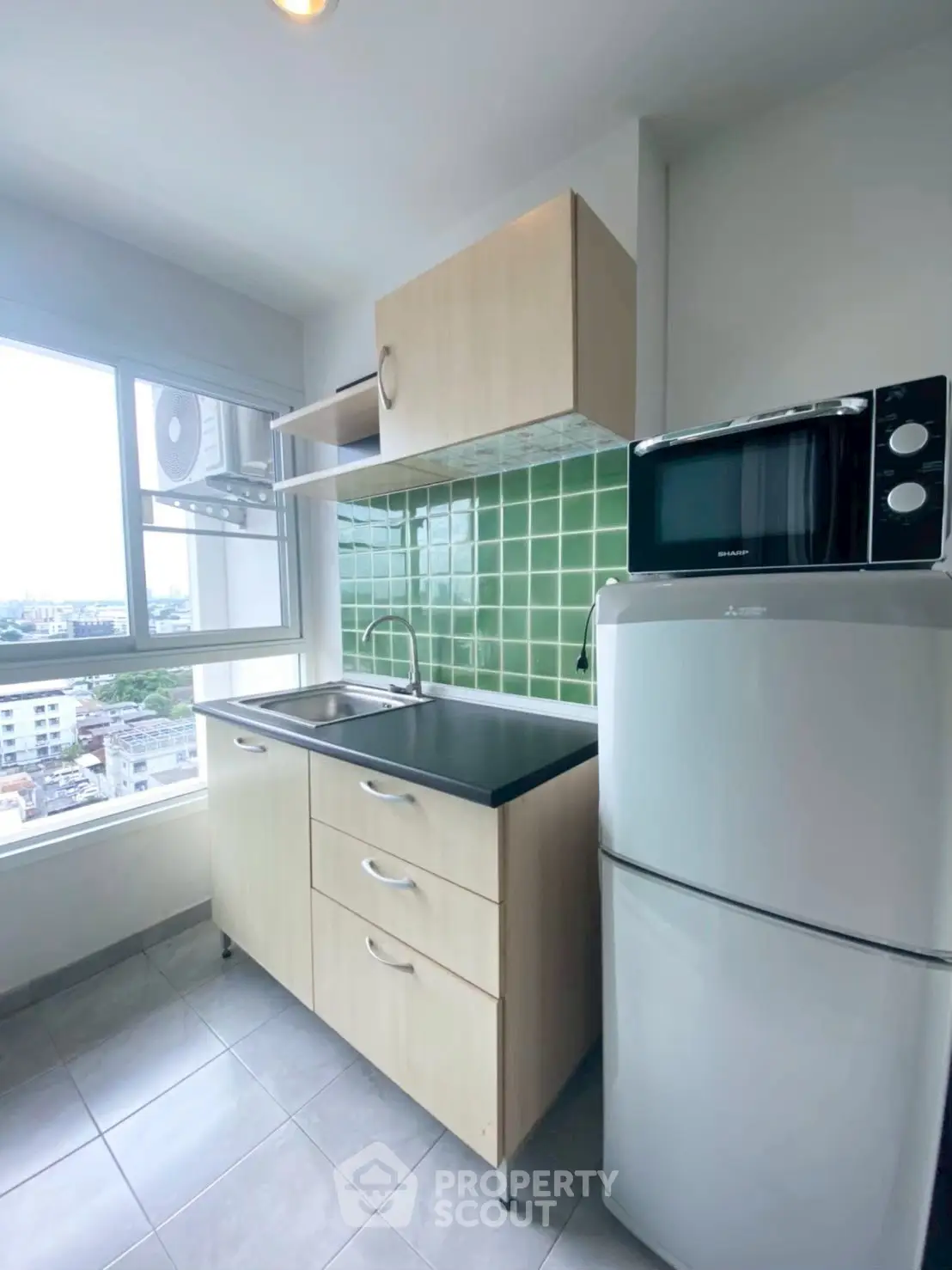 Modern kitchen with green tile backsplash, compact fridge, and microwave in a bright apartment.