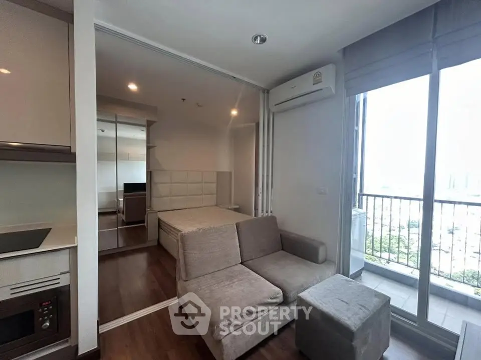 Modern studio apartment with cozy living area and balcony view, featuring sleek kitchen and comfortable furnishings.