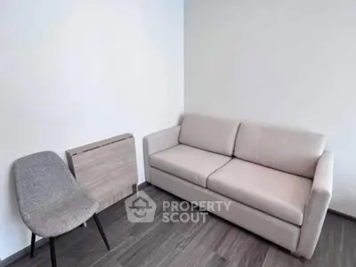 Modern minimalist living room with sleek sofa and stylish chair on wooden flooring.