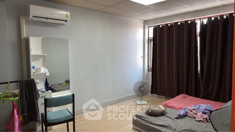 Cozy bedroom with minimalist decor, featuring a bed, chair, and air conditioning unit.