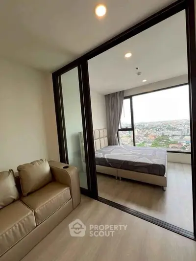 Modern bedroom with floor-to-ceiling windows offering stunning city views, adjacent to cozy living area.