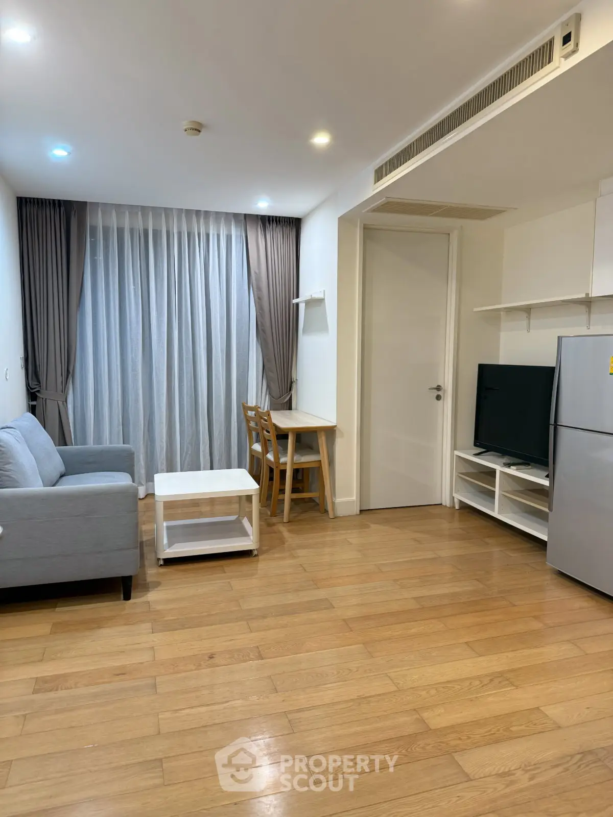 Modern living room with wooden flooring, cozy sofa, and sleek TV setup in a stylish apartment.