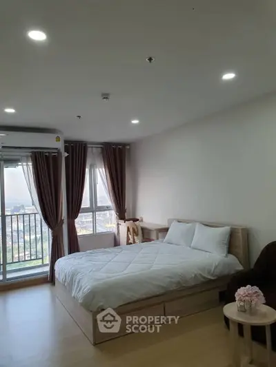 Spacious bedroom with balcony and city view, modern decor and natural light.