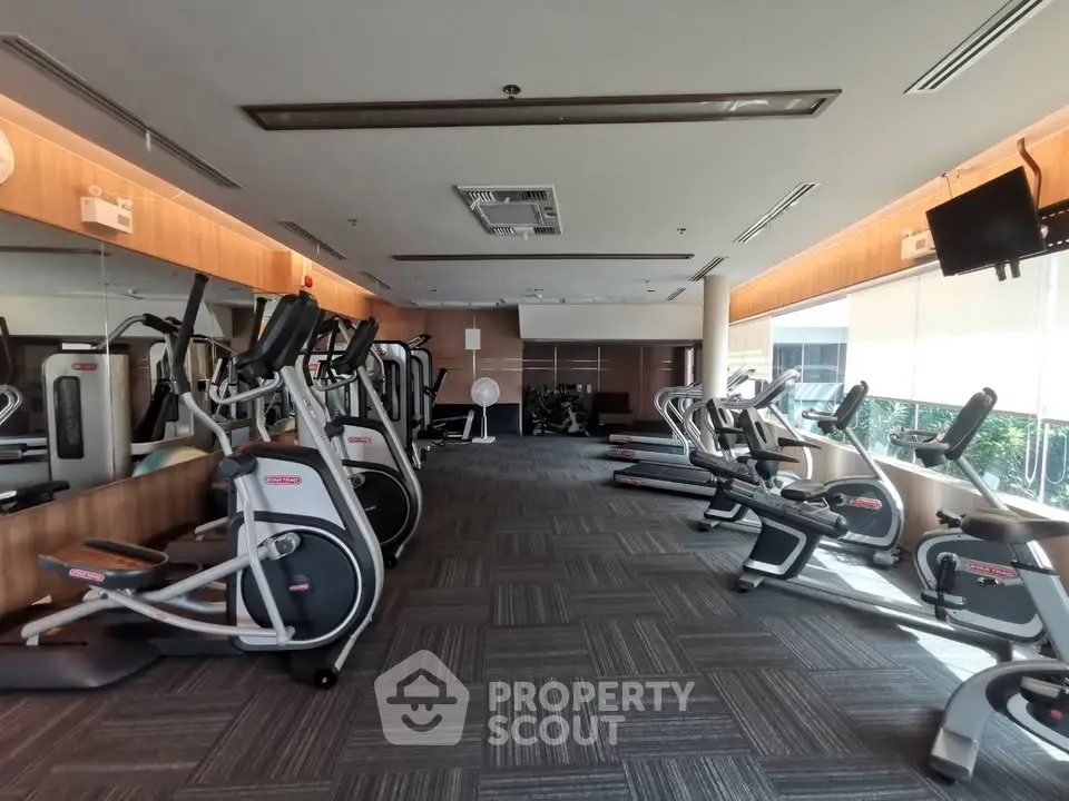 Spacious gym with modern equipment and large windows for natural light.
