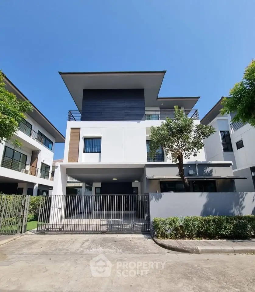 Modern three-story house with sleek design and gated entrance in a serene neighborhood.