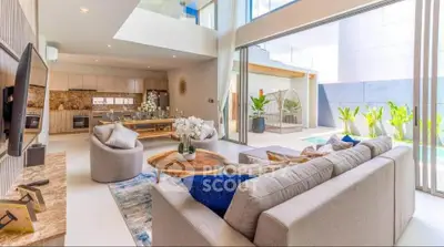 Luxurious open-plan living room with modern kitchen and pool view, featuring elegant decor and abundant natural light.