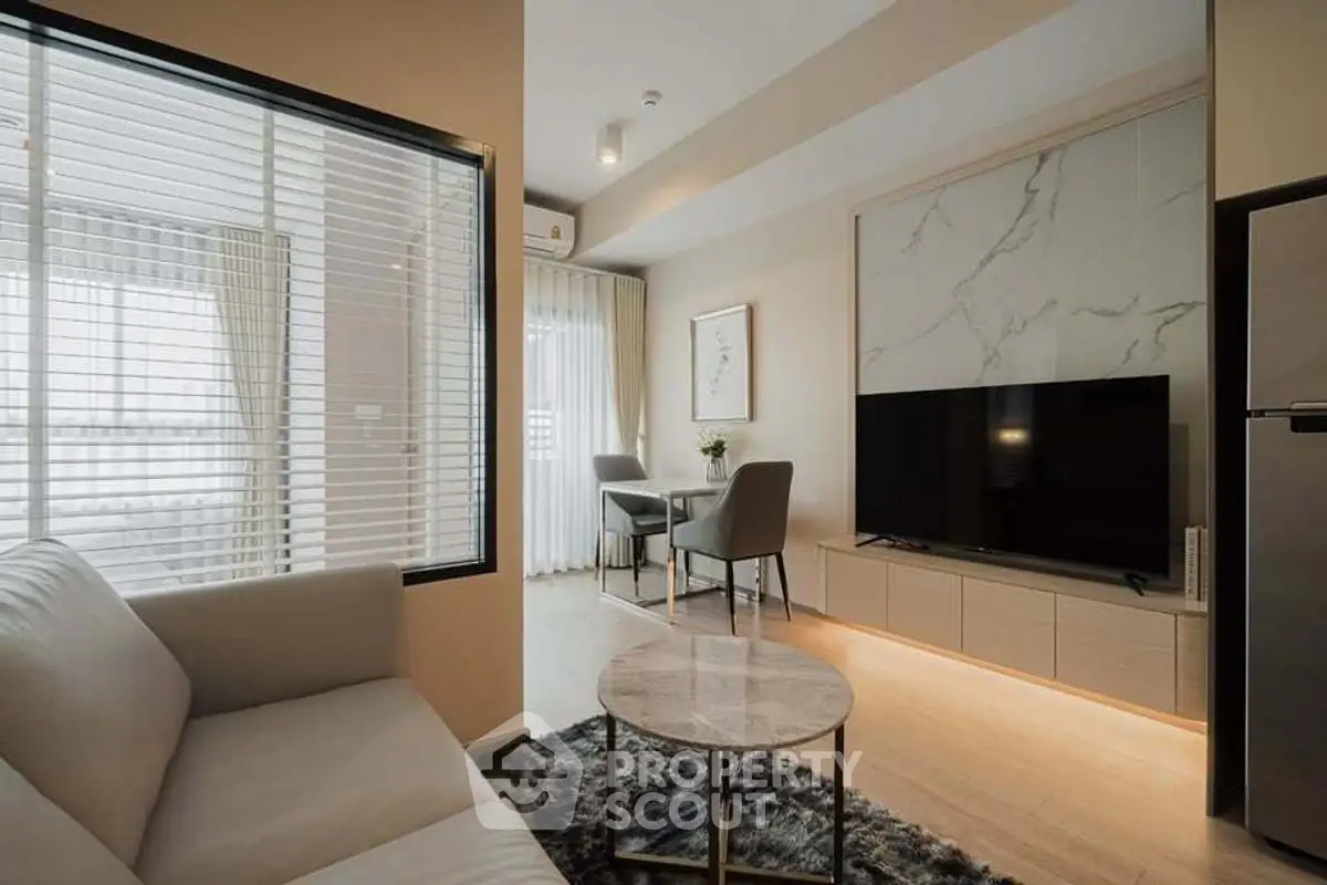 Modern living room with sleek furniture and large TV, featuring a cozy dining area by the window.