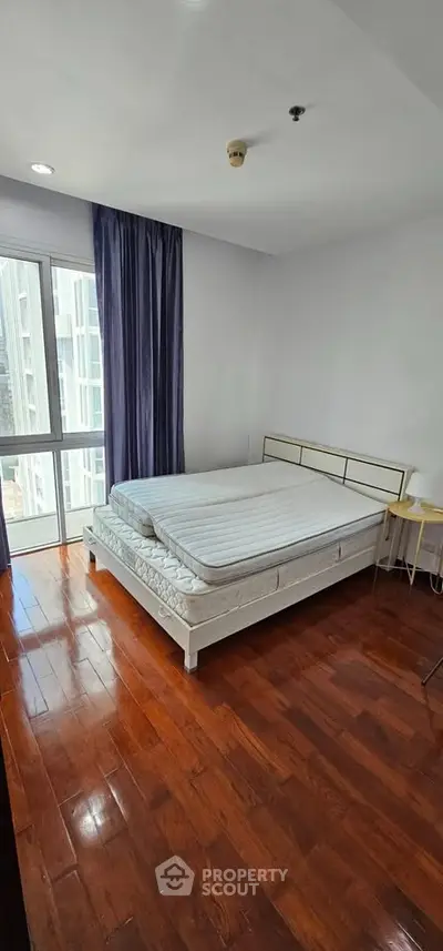 Spacious bedroom with large window and wooden flooring in modern apartment