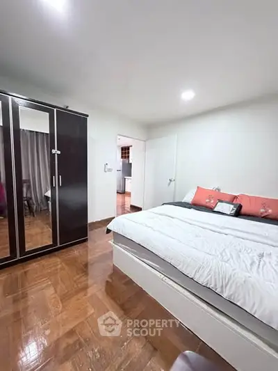 Spacious bedroom with wooden flooring and modern wardrobe in a cozy apartment.
