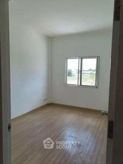 Bright empty room with wooden flooring and a window view, perfect for customization.