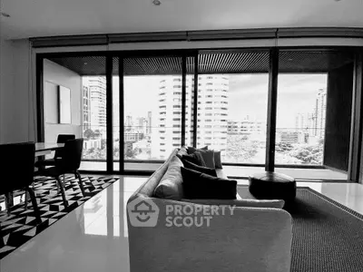 Modern living room with floor-to-ceiling windows offering stunning city views, sleek furniture, and stylish decor.