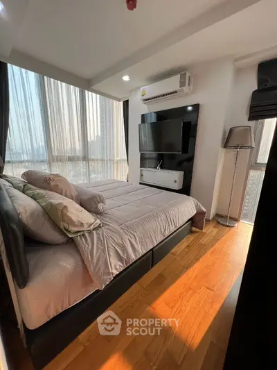 Modern bedroom with large windows and wooden flooring, featuring a sleek TV setup and air conditioning.