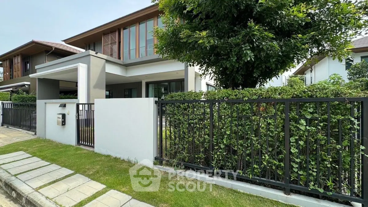 Modern two-story house with lush garden and sleek fence in a serene neighborhood.
