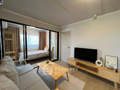 Modern living room with cozy sofa, wooden coffee table, and TV unit, adjacent to a glass-enclosed bedroom.