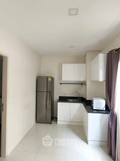 Modern kitchen with sleek cabinets, stainless steel fridge, and microwave in a compact layout.