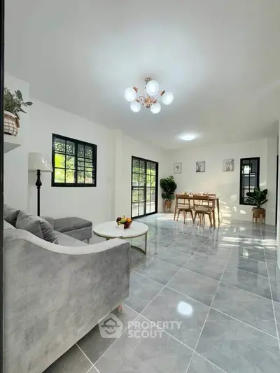 Spacious modern living room with elegant decor and dining area, featuring large windows and stylish lighting.