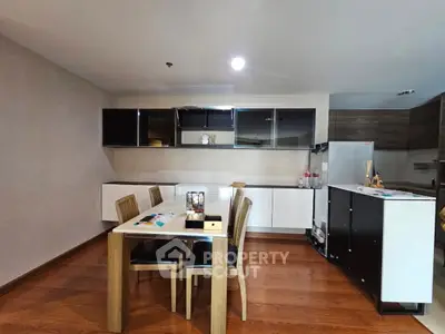 Modern kitchen with dining area featuring sleek cabinets and wooden flooring.
