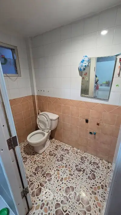 Cozy bathroom with tiled walls and floor, featuring a toilet and mirror.