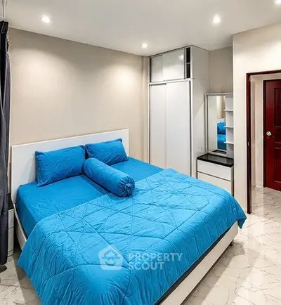 Spacious bedroom with modern design and vibrant blue bedding, featuring sleek storage solutions.