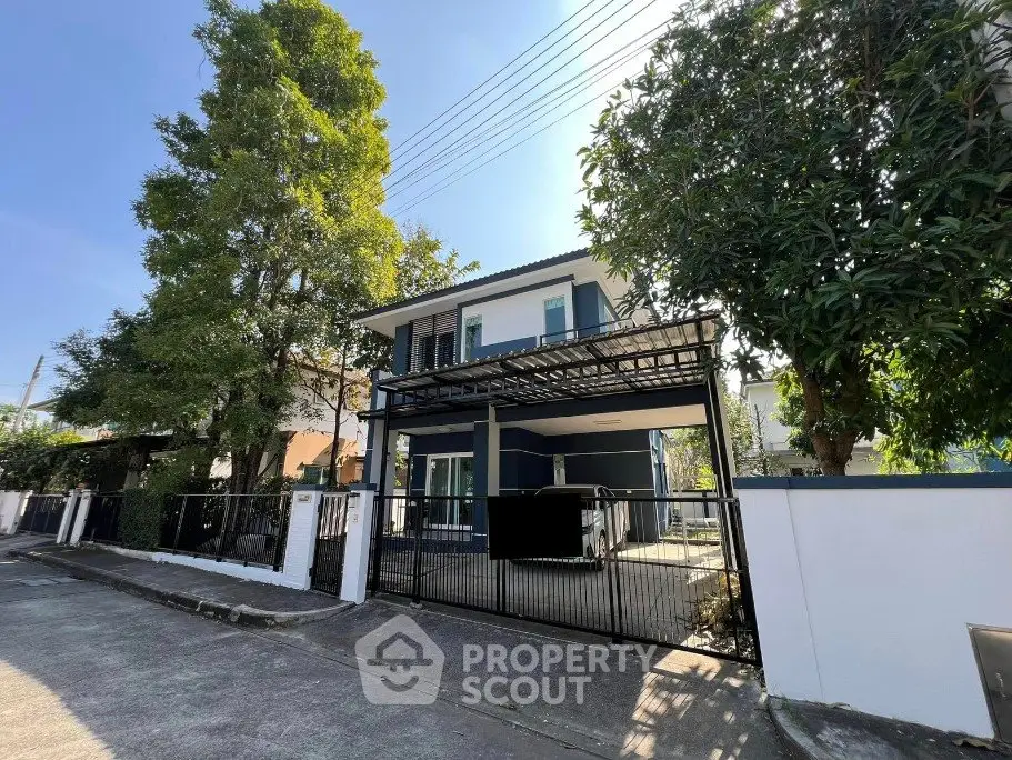 Modern two-story house with gated entrance and lush greenery in a serene neighborhood.