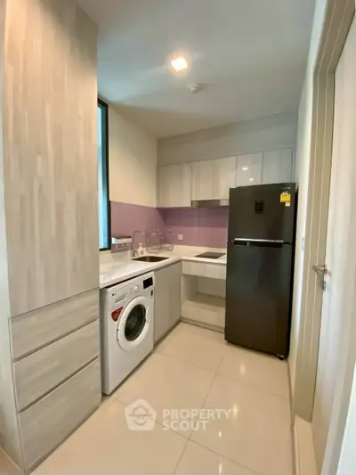 Modern kitchen with sleek cabinetry, washing machine, and stainless steel fridge in compact layout.